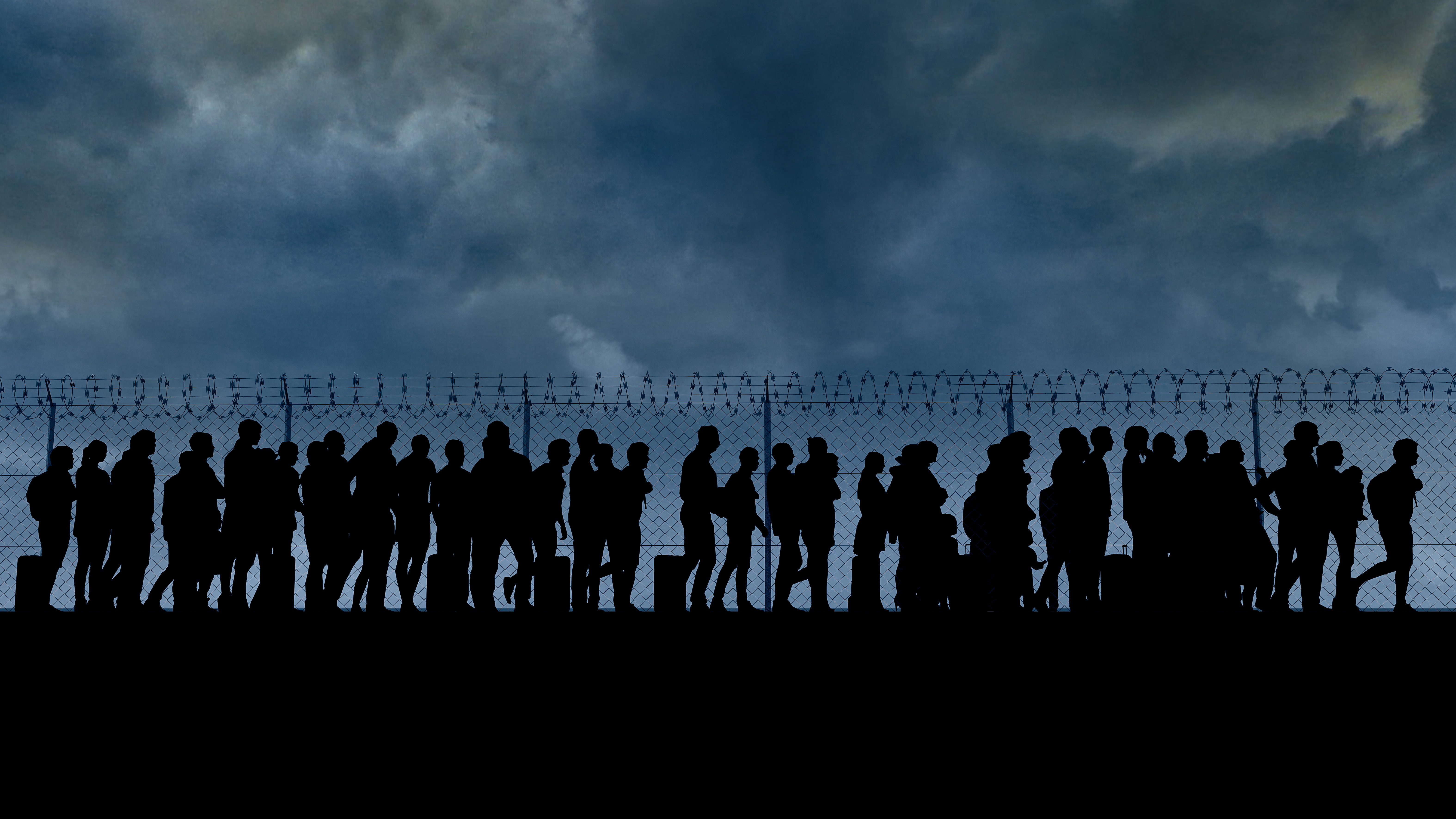 Picture of migrants on a line near a fence